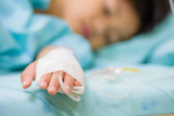 Closeup kid hand  sleeps on a bed in hospital with saline intravenous, selective focus. — Stock Photo, Image