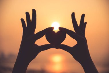 Yakın up ve günbatımı sırasında kırmızı kalp tutan el silüeti 