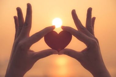 Yakın up ve günbatımı sırasında kırmızı kalp tutan el silüeti 