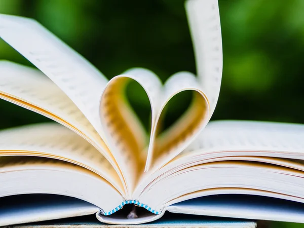 Book on table in garden with top one opened and pages forming heart shape — Stock Photo, Image