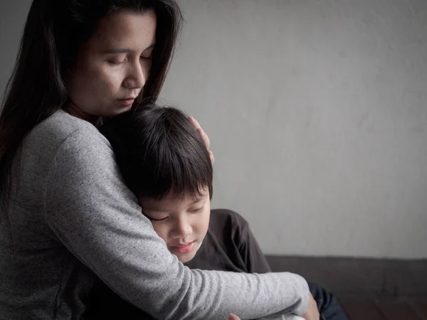 Sad little boy being hugged by his mother at home.