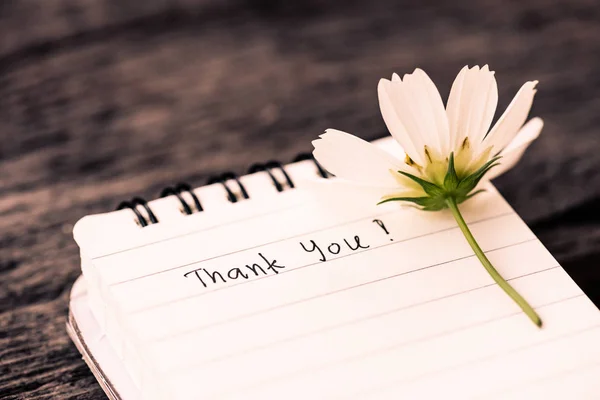 Thank You text on a white page note book with romantic white flower