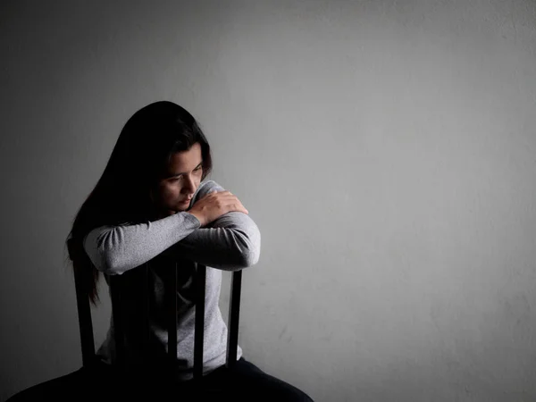 Depressed broken hearted woman sitting alone on a wooden chair in dark room at home. — Stock Photo, Image