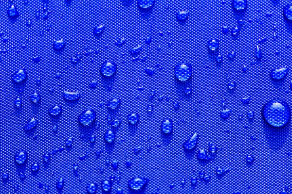 Fermer Modèle gouttes d'eau sur un fond en tissu imperméable bleu. Concept de Journée mondiale de l'eau . — Photo