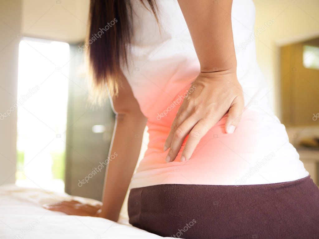 Young woman feeling pain in her back on the bed at home. 