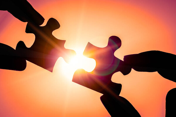 Silhouette of closeup woman's hand connecting a piece of jigsaw puzzle over sunlight effect. symbol of association and connection concept.