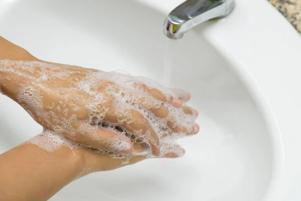 Mujer lavándose las manos con jabón debajo del grifo con agua en el baño . — Foto de Stock