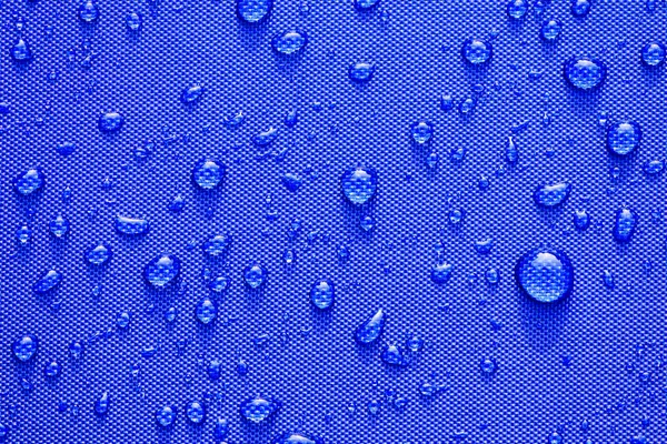 Gros plan Modèle de gouttes d'eau sur un fond en tissu imperméable bleu . — Photo