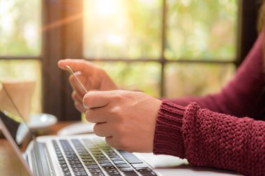 Bir kredi kartı tutan ve online alışveriş için dizüstü bilgisayar kullanan genç ve güzel kadının elleri. 
