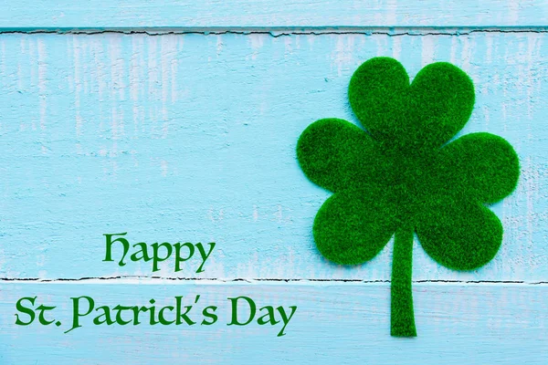 Happy St Patricks Day message and a lot of green paper clover leaf on Pastel white and blue wooden table background texture.