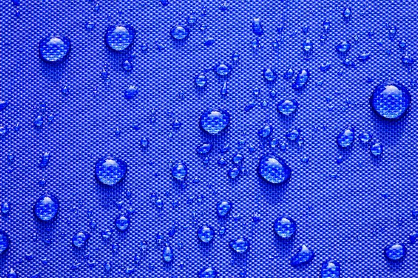 Fechar o padrão de gotas de água sobre um fundo de pano impermeável azul . — Fotografia de Stock