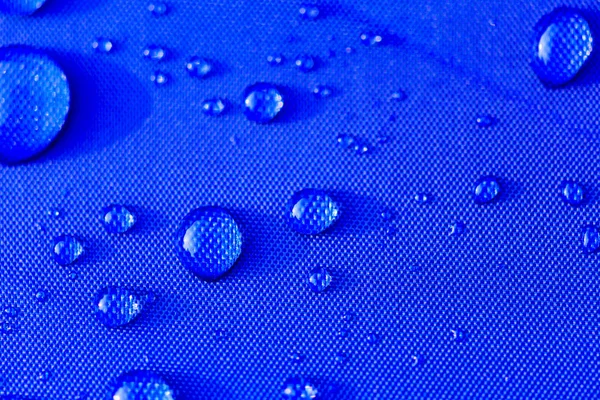 Närbild av vatten droppar mönster över en blå vattentät duk bakgrund. Världen vattendagen koncept. — Stockfoto