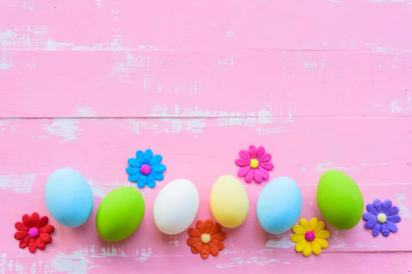 Satır Paskalya yumurtaları parlak pembe ve Beyaz ahşap arka plan üzerinde renkli kağıt çiçeklerle. — Stok fotoğraf
