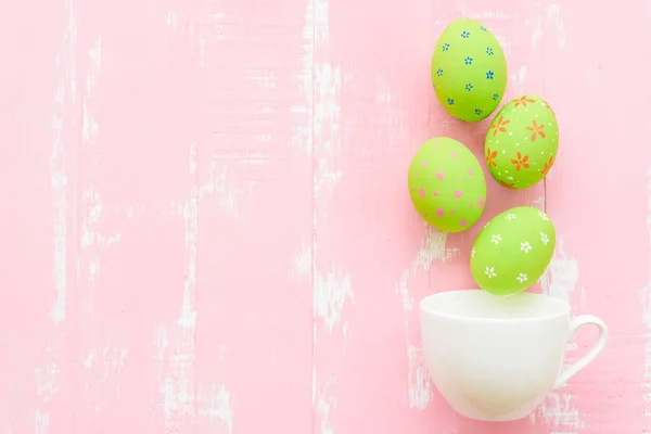 Mutlu Paskalyalar! Parlak pembe ve yeşil ahşap arka plan üzerinde beyaz fincan satır renkli Paskalya yumurtaları dağılın. — Stok fotoğraf
