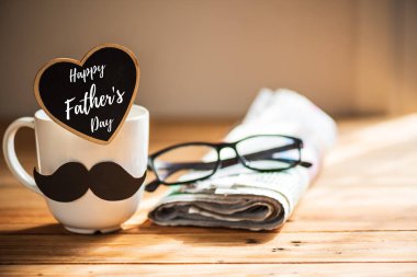 Mutlu babalar günü kavramı. kahve fincanı siyah kağıt bıyıklı, kalp etiketi ile mutlu babalar günü metin ve gazete, ahşap masa arka plan üzerinde gözlük.