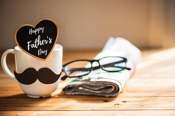 幸せな父親の日のコンセプトです 木製のテーブルの背景に黒い紙口ひげとコーヒー カップ 幸せな父の日のテキストと新聞 ハート メガネします — ストック写真