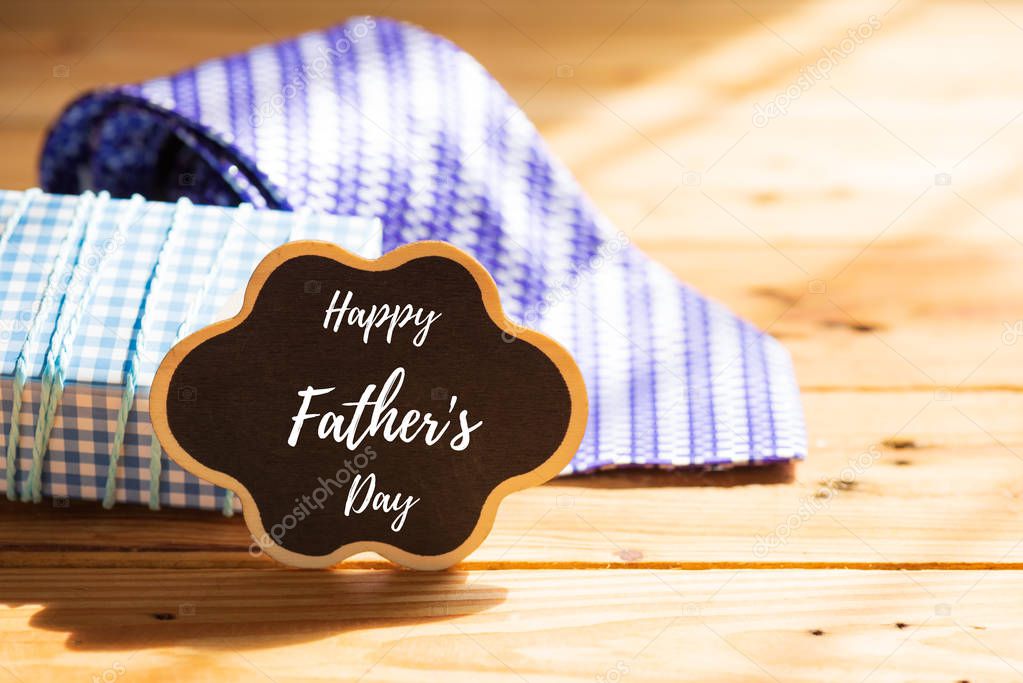 Happy fathers day concept. Purple tie and gift box with Happy father's day tag on wooden table background.