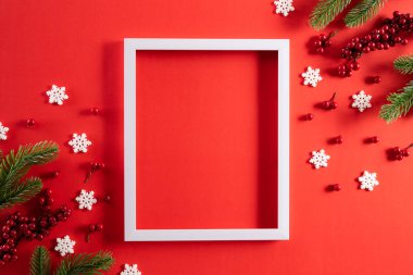 Noel tatilleri kompozisyonu. Noel ağacı süslemesi ve yeşil pastel arka planda kırmızı böğürtlenli beyaz resim çerçevesinin üst görünümü..