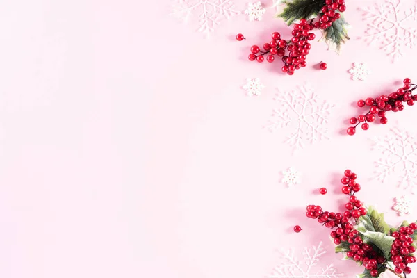 Christmas background concept. Top view of Christmas ball with snowflakes and red berries on light pink pastel background.