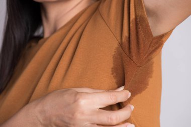 Hiperhidrozis Terleme ile yakın çekim Asyalı kadın. Gri arka plana karşı giysileri üzerinde ter lekeli genç Asya kadın. Sağlık konsepti.