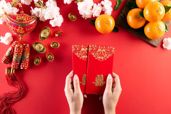 Çin Yeni Yıl Festivali dekorasyonu. El ele tutuşan kadın ya da kırmızı paket, kırmızı arka planda turuncu ve altın külçeler. Çin karakterleri Fu servet, servet, para akışı anlamına gelir.. — Stok fotoğraf
