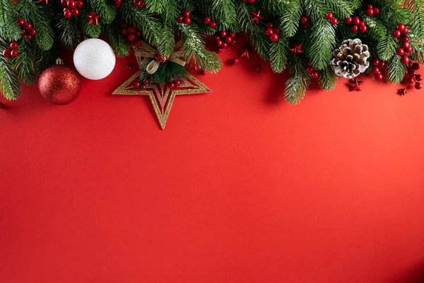 Koncepcja Bożego Narodzenia. Widok z góry pudełko świąteczne czerwone kulki z gałązek świerkowych, szyszki sosnowe, czerwone jagody gwiazda i dzwon na czerwonym tle. — Zdjęcie stockowe