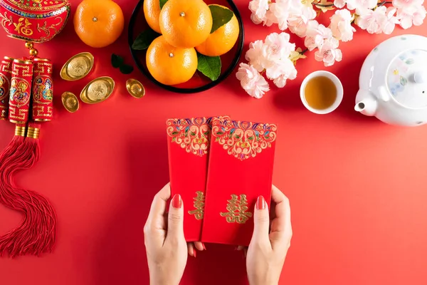 Çin Yeni Yıl Festivali dekorasyonu. El ele tutuşan kadın ya da kırmızı paket, kırmızı arka planda turuncu ve altın külçeler. Çin karakterleri Fu servet, servet, para akışı anlamına gelir.. — Stok fotoğraf