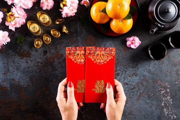 Kínai újévi fesztivál dekorációk. Női kéz tartó pow vagy piros csomag, narancs és arany ingots fekete kő textúra háttér. Kínai karakterek Fu azt jelenti szerencse szerencse, gazdagság, pénzáramlás. — Stock Fotó