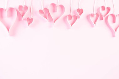 Pembe kağıt kalpler açık pembe renkli kağıt arka planda iplerde sallanıyor. Aşk ve Sevgililer Günü konsepti.