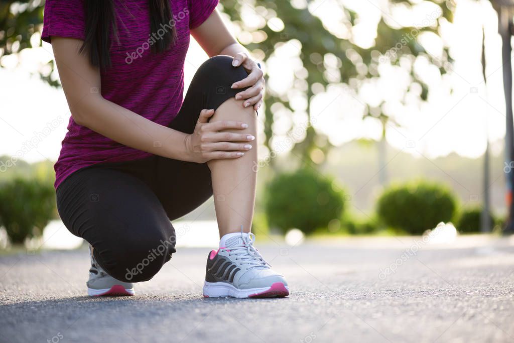 Young fitness woman runner feel pain on her knee in the park. Ou