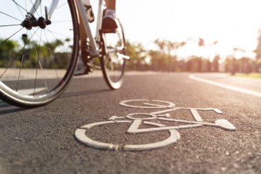 Yolda bisiklet logosu görüntüsünü kapatın. Atletik kadın bisikletçi bacakları sabah arka planda dağ bisikletine biniyor..