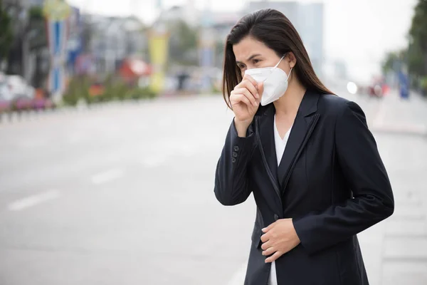 Close up of a businesswoman in a suit wearing Protective face mask and cough, get ready for Coronavirus and pm 2.5 fighting against beside road in background.