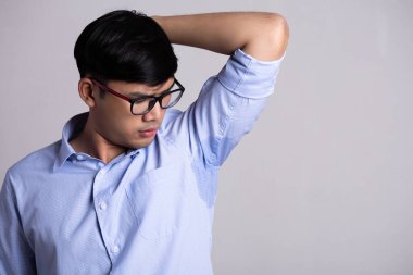 Hiperhidrozlu Asyalı adam terliyor. Giysilerinde gri arka planda ter lekesi olan Asyalı genç bir adam. Sağlık hizmetleri kavramı.