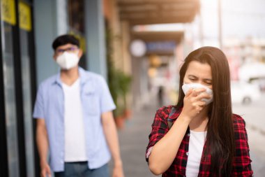 Kadın ve erkek koruyucu yüz maskesi takıp öksürmeye, Coronavirus 'a ve 2.5.' deki açık hava alışveriş merkezinin arka planında kavga etmeye hazır olun..