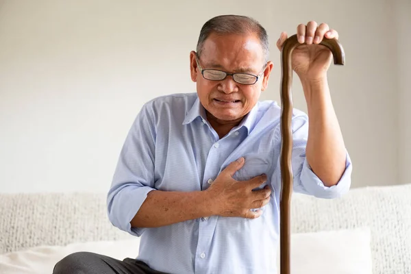 アジアの老人はソファに座って 自宅で心臓発作に苦しんでいます シニアヘルスケアコンセプト — ストック写真