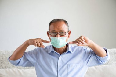 Hasta Asyalı yaşlı adam koruyucu yüz maskesi takıyor ve baş ağrısı çekiyor, Coronavirus 'a hazır olun ve 2.5. Dövüş, evdeki kanepede oturmak. Kıdemli sağlık hizmeti kavramı.