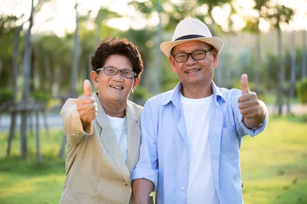 A happy senior couple asian old man and woman with thumbs up smiling and laughing in the garden, happy marriage. Senior healthcare and relationship concept.