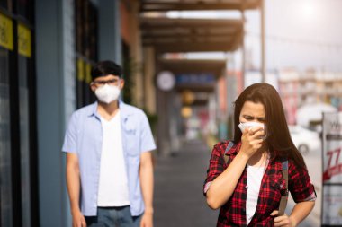 Kadın ve erkek koruyucu yüz maskesi takıp öksürmeye, Coronavirus 'a ve 2.5.' deki açık hava alışveriş merkezinin arka planında kavga etmeye hazır olun..