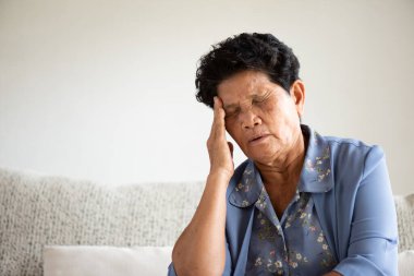 Asyalı yaşlı kadın kanepede oturuyor ve evde baş ağrısı çekiyor. Kıdemli sağlık hizmeti kavramı.