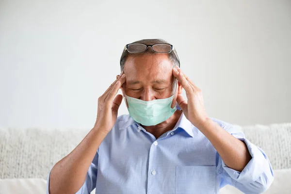 保護顔のマスクを着用し 頭痛を持っている病気のアジアの老人は 自宅でソファに座って コロナウイルスや午後2時半の戦いの準備をしてください シニアヘルスケアコンセプト — ストック写真