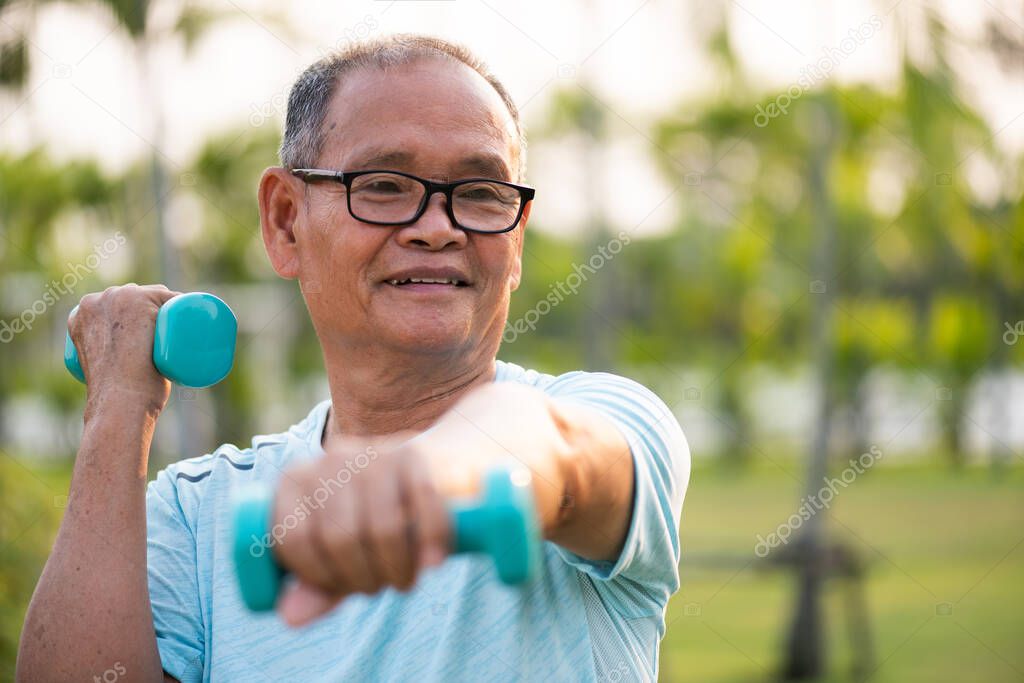 Asian old man doing physical exercise outdoor with dumbbells. Be healthy and strong, work on the muscles. Senior healthcare and sport concept.