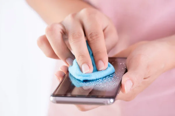 Closeup woman hands cleaning the smartphone screen with a fiber cloth from dirt dust and virus, against Coronavirus or Corona virus disease (Covid-19). Healthcare and disinfection concept.