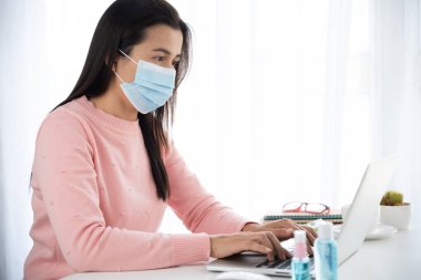 İş kadını eli bilgisayarla evden iş yapıyor. Akıllı telefon faresi, dezenfektan jeli, yüz maskesi ve Coronavirus hastalığını önlemek için alkol spreyi (COVID-19). Sağlık bakımı dezenfeksiyon konsepti.
