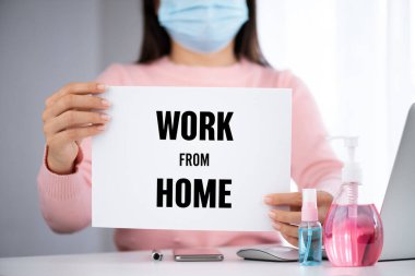 İş kadını elinde ev mesajlarıyla beyaz kağıt tutuyor. Coronavirus hastalığını önlemek için dizüstü bilgisayar faresi akıllı telefonu, dezenfektan jeli, tıbbi yüz maskesi ve alkol spreyi (COVID-19).