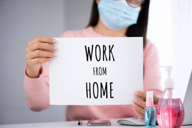İş kadını elinde ev mesajlarıyla beyaz kağıt tutuyor. Coronavirus hastalığını önlemek için dizüstü bilgisayar faresi akıllı telefonu, dezenfektan jeli, tıbbi yüz maskesi ve alkol spreyi (COVID-19).
