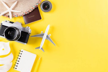Yaz tatili ve tatil konsepti. Plaj aksesuarları retro film kamerası, güneş gözlükleri, denizyıldızı, plaj şapkası, uçak ve deniz kabuğu sarı arka planda..