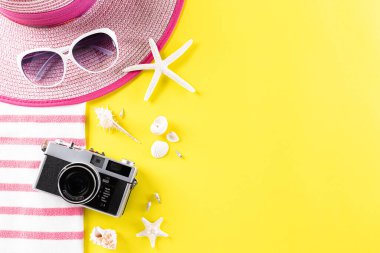 Yaz tatili, seyahat ve tatil konsepti. Retro film kamerası, güneş gözlüğü, denizyıldızı, plaj şapkası ve deniz kabuğu sarı arka planda, fotokopi alanı ile düz yatıyordu..
