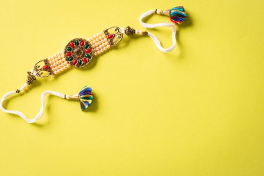 Raksha Bandhan, sarı arka planda güzel Rakhi ve Pirinç Taneleri olan Hint festivali. Geleneksel Hint bilekliği kız kardeşler ve erkek kardeşler arasındaki aşkın sembolüdür..