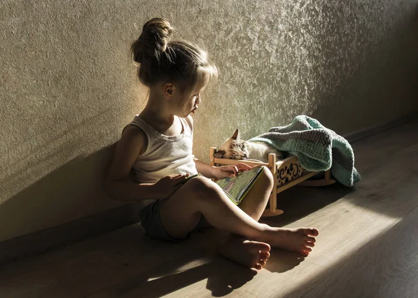 A girl is reading a fairy tale from a book to a cat in a crib Royalty Free Stock Images