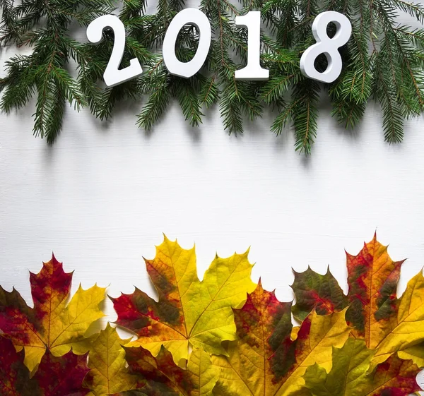 Branches d'épinette avec chiffres 2018 et feuilles jaunes d'érable tombées sont répartis sur les côtés opposés de la table blanche — Photo